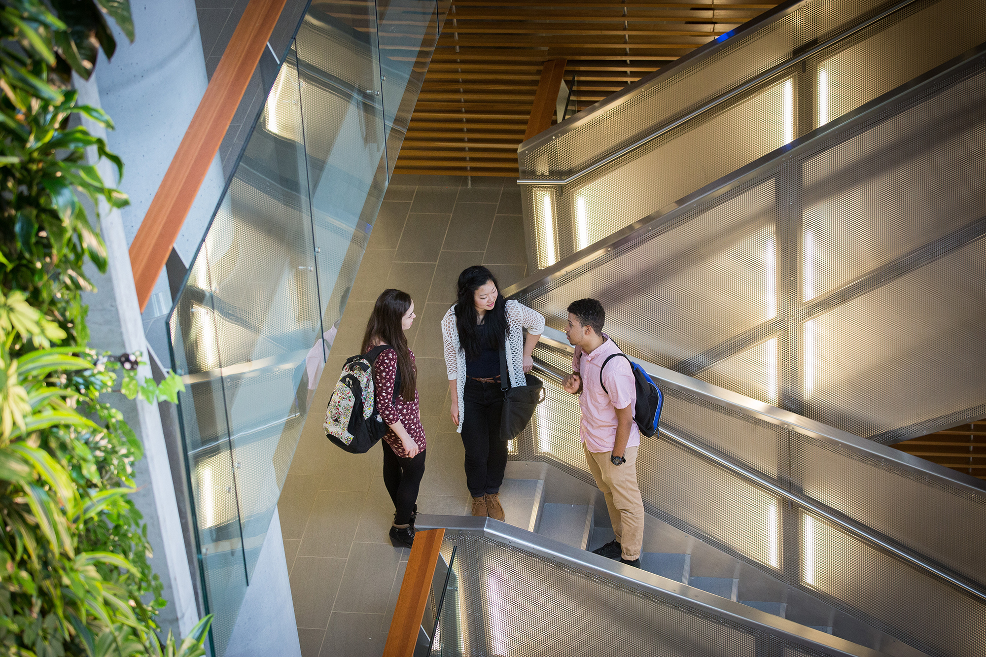 Un étudiant et deux étudiantes debout sur un escalier.