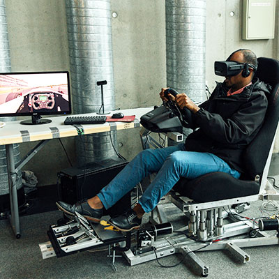 Une personne dans une chaise qui porte un casque de réalité virtuelle et qui tient un volant.