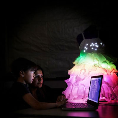 Une étudiante et enseignante qui travaillent sur un ordinateur portable avec une robe illuminée en arc-en-ciel dans l'arrière plan.