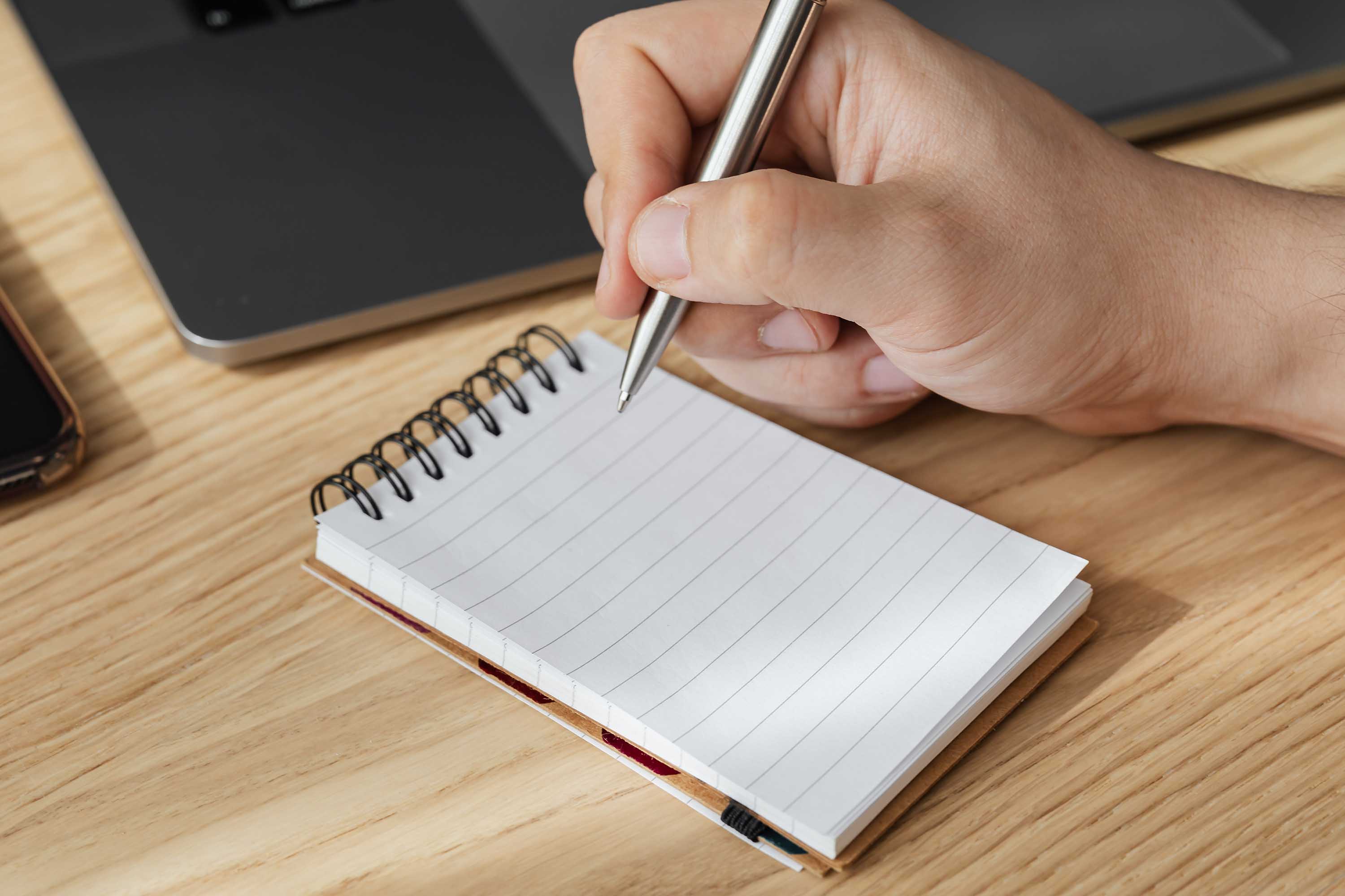Une main tient un stylo au-dessus d'un carnet de notes