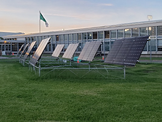 Image of eight solar cells on a lawn next to a building with lots of windows